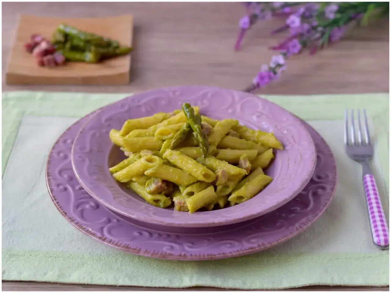 Piatto di pasta con asparagi e speck, guarnito con un asparago intero.