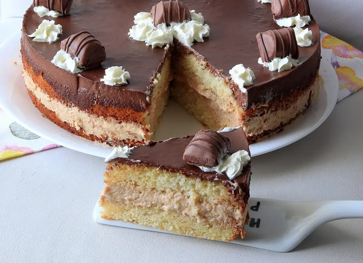 Deliziosa torta Kinder Bueno con strati di pan di Spagna, crema e copertura al cioccolato, decorata con panna e pezzi di Kinder Bueno.