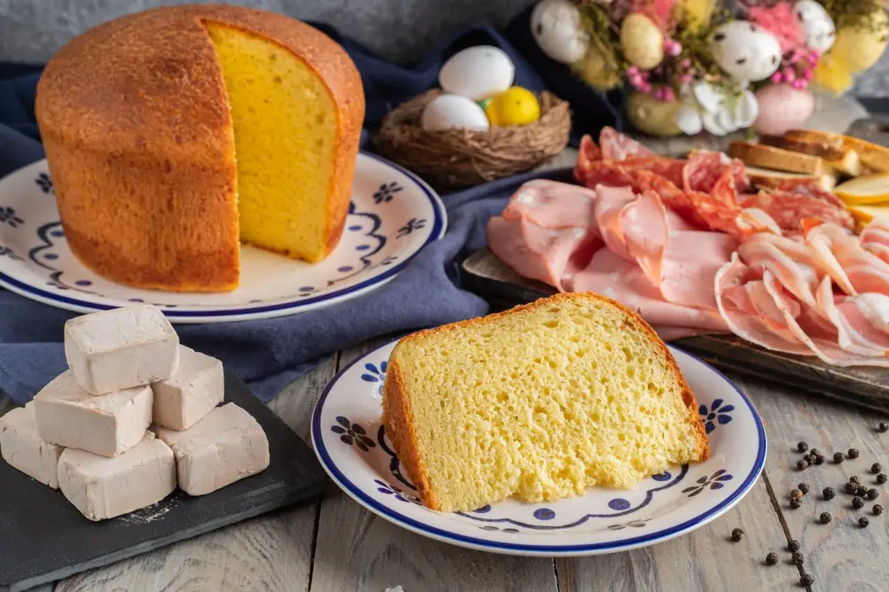 Fetta di crescia di Pasqua marchigiana, soffice e dorata, accanto a salumi, uova e lievito.