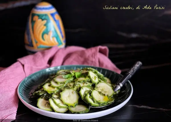 Fette di zucchine marinate crude, condite con erbe aromatiche e olio. Un contorno fresco e leggero, perfetto per l'estate.