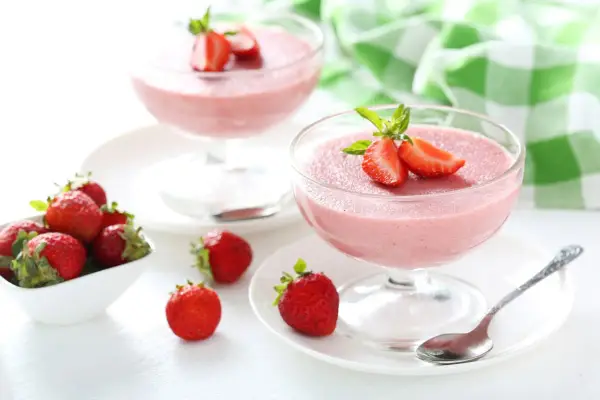 Deliziosa mousse di fragole in coppette di vetro, guarnita con fragole fresche e menta. Accanto, fragole in una ciotola bianca.