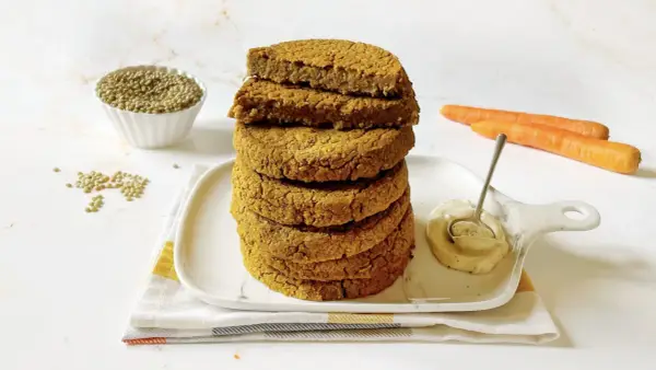 Impilati hamburger di lenticchie dorati, con lenticchie secche, carote e una salsa cremosa in un piatto.