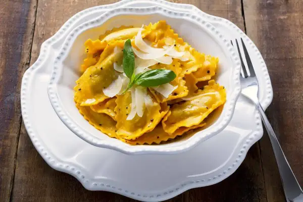 Un piatto invitante di tortelli di zucca, guarniti con scaglie di parmigiano e una fogliolina di basilico, pronti per essere gustati.
