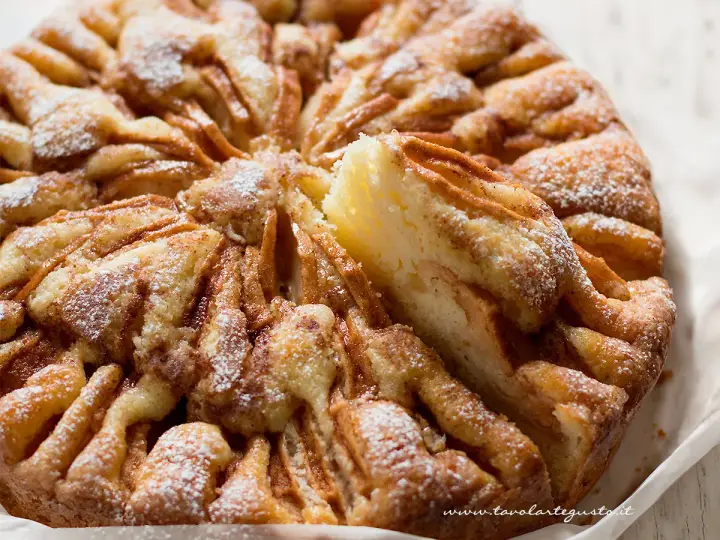 Una deliziosa torta di mele, cosparsa di zucchero a velo, con una fetta appena tolta che rivela la morbidezza dell'interno.