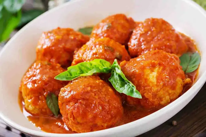 Polpette al sugo succulente in un piatto bianco, guarnite con foglie di basilico fresco. Un classico della cucina italiana.