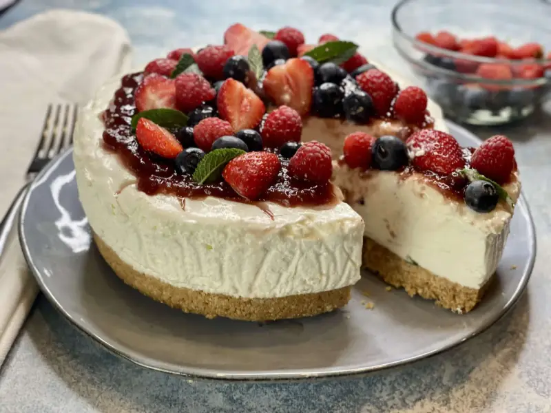 Deliziosa torta fredda allo yogurt, guarnita con fragole, lamponi, mirtilli e una colata di marmellata. Perfetta per un dessert estivo.